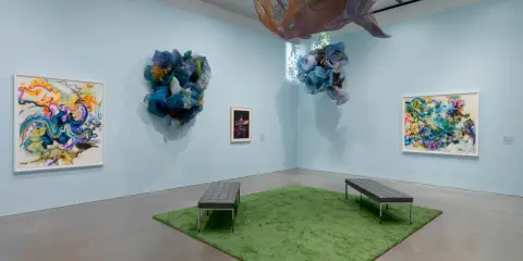 Abstract paintings and fabric sculptures adorn the walls of the Lanoue Gallery, with benches placed on a patch of artificial grass.