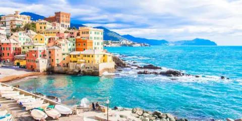 Case colorate a picco sul mare turchese, barche ormeggiate e un promontorio roccioso: un angolo di Genova che ricorda le sue spiagge più belle.
