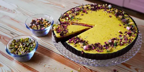 Wyjątkowa tarta pistacjowa, udekorowana płatkami róż i orzechami, kusi swoim wyglądem. Obok miseczki z pistacjami.