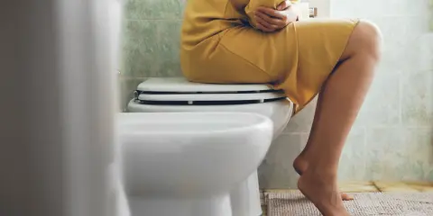 Kobieta siedzi na toalecie, trzymając się za brzuch. Czy to objaw anurii?