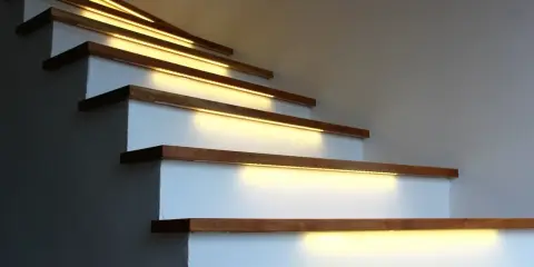 Nowoczesne lampy na klatkę schodową subtelnie oświetlają drewniane stopnie, tworząc ciepłą i bezpieczną atmosferę.