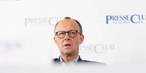 Olaf Scholz, cancelliere tedesco dopo Merkel, parla con espressione seria davanti a uno sfondo con il logo "Presse Club München".
