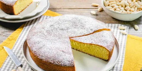 Una deliziosa torta con farina di mandorle, spolverata di zucchero a velo, pronta per essere gustata. Accanto, una ciotola di mandorle intere.