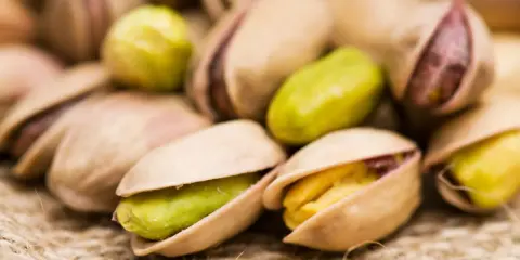Un mucchio di pistacchi, alcuni aperti rivelano il loro interno verde e giallo. Attenzione, i pistacchi fanno ingrassare!