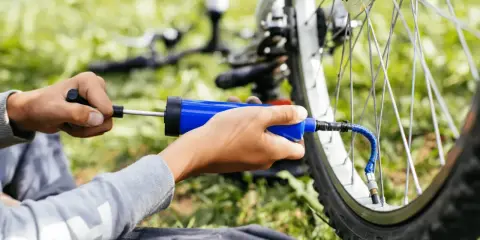 Ręce pompują rower na stacji. Niebieska pompka podłączona do wentyla koła, gotowa do akcji.