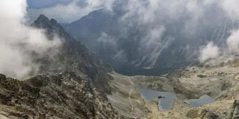 Widok na skaliste zbocza i dwa jeziora w Tatrach, rysy od strony polskiej. Mgła otula szczyty.