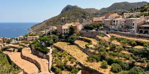 Terrassierte Felder und Häuser schmiegen sich an die Hänge des Tramuntana Gebirges, mit dem blauen Meer im Hintergrund.