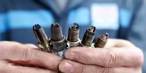 Pięć zużytych świec zapłonowych w dłoniach mechanika, kluczowe dla prawidłowego doboru świec zapłonowych do silnika.