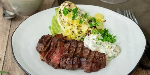 En saftig grillad ryggbiff serveras med krispig sallad, grillad kål och en krämig sås.