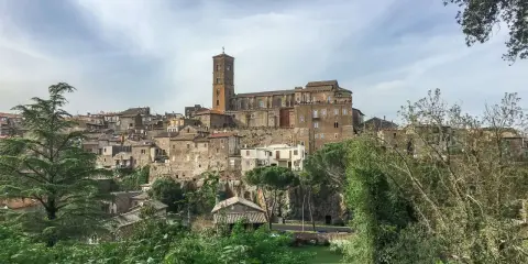 Panoramica dell'antico borgo di Sutri, con le sue case in pietra arroccate su una collina e una maestosa cattedrale con campanile.