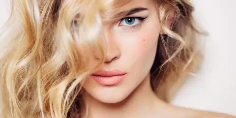 Mujer rubia con ondas, delineado de ojos y labios rosados. Un ejemplo de trucos de belleza para realzar la mirada.