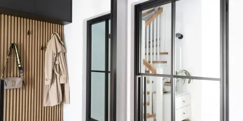 Nowoczesny wiatrołap inspiracje: drewniana boazeria, płaszcz i torebka wiszą na haczykach, obok schody z białymi balustradami.