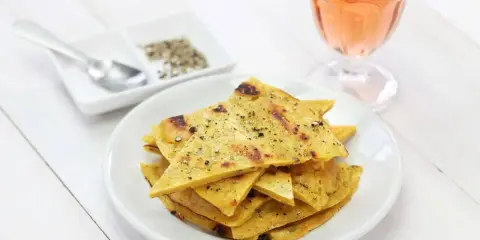 Une assiette de socca à la poêle, coupée en triangles et saupoudrée de poivre, à côté d'un verre de rosé.