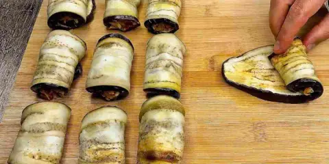 Involtini di melanzane pronti per essere infornati. Una mano sta arrotolando l'ultima fetta di melanzana grigliata.