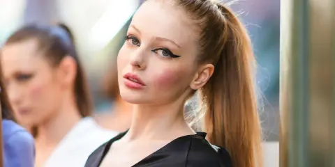 Modelo con delineado cat eye dramático y labios rosados, su cabello recogido en una coleta alta.