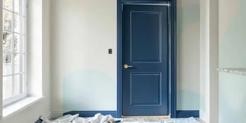 Peinture porte intérieure bleu marine, avec des touches de bleu clair sur le mur. Des rouleaux et pinceaux sont au sol, prêts pour la prochaine étape.