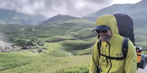 Uśmiechnięty turysta w żółtej kurtce z plecakiem w malowniczych rumuńskich górach.