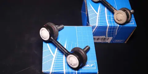 Due biellette auto SKF, componenti essenziali per la stabilità del veicolo, posizionate su scatole blu.