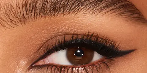 Ojo con pestaña larga y ceja poblada, delineado negro con un sutil eyeliner difuminado en el párpado superior.