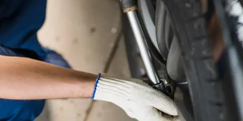 Ręka w białej rękawiczce dokręca śrubę kluczem przy kole samochodu.