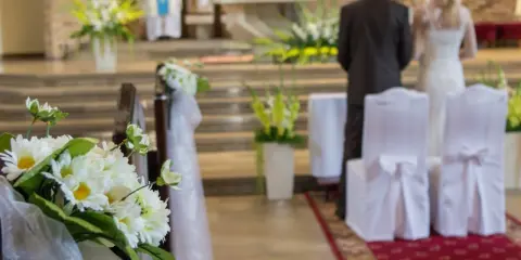 Kwiaty zdobią kościelną nawę. Para młoda stoi przy ołtarzu, przygotowując się do ślubu kościelnego jednostronnego.