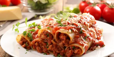 Pyszne cannelloni z mięsem mielonym, polane sosem pomidorowym i posypane parmezanem, na talerzu z pomidorami i sałatką.