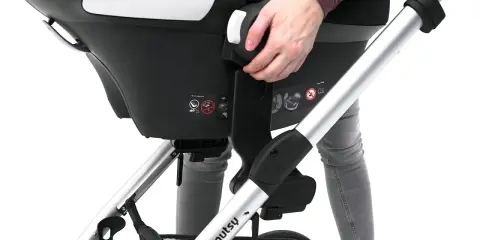 Ręka naciska dźwignię, pokazując, jak wyjąć adaptery z fotelika samochodowego.