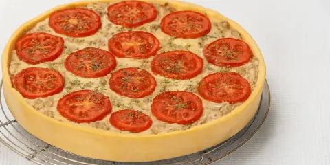 Une délicieuse quiche au thon, garnie de rondelles de tomates fraîches et d'herbes, prête à être dégustée.
