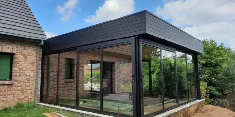 Moderne véranda toit plat avec puits de lumière, offrant une vue panoramique sur le jardin. L'extension en verre et métal s'intègre parfaitement à la maison en briques.