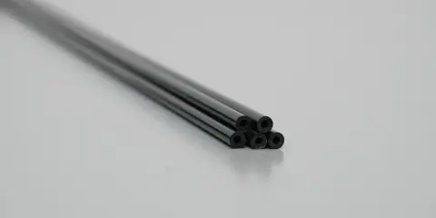 Mehrere schwarze, glänzende rundrohr kunststoff Stäbe liegen auf einer grauen Fläche.