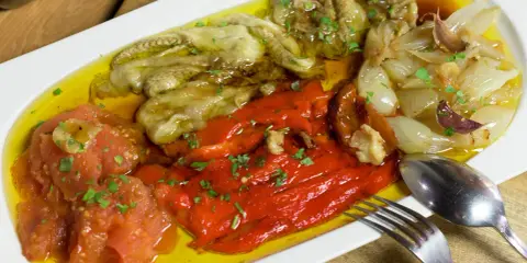 Deliciosa escalivada al forn con pimientos rojos, berenjenas, tomates y cebollas asadas, regada con aceite de oliva y perejil picado.
