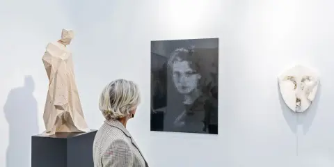 A woman views a collection of art, including a wooden sculpture and a portrait, appreciating art as an asset class.