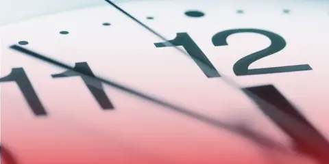 Zbliżenie na tarczę zegara. Wskazówki zbliżają się do godziny 12. Czy to już koniec pracy, czy początek nowego dnia? Liczba godzin pracy 2026.