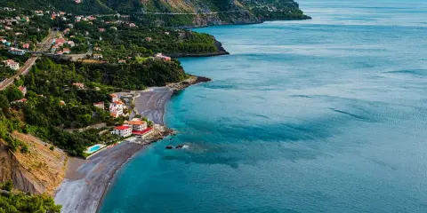 Villaggio costiero con case bianche e rosse affacciato su una spiaggia di ciottoli scuri e mare blu intenso. Le **basilicata spiagge** offrono panorami mozzafiato.