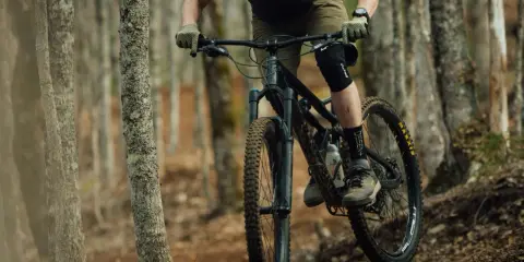Rowerzysta w kasku i ochraniaczach pokonuje leśny szlak na rowerze górskim, jednym z wielu rodzajów rowerów do jazdy terenowej.