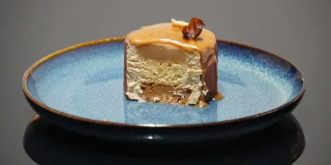 Tranche d'entremet aux couches aériennes, surmontée d'un glaçage caramel et d'une noisette croquante. Le biscuit noisette pour entremet offre une texture légère et savoureuse.