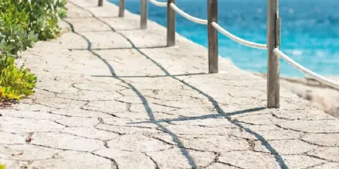 Camino de piedra con barandilla y mar azul. Un ejemplo de cómo hacer hormigón impreso para exteriores.