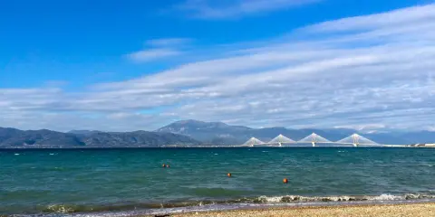 Spokojne morze i plaża w Grecji w styczniu. W oddali widać most Rio-Antirio i góry.