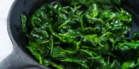 Spinaci freschi e lucidi che sfrigolano in una padella di ghisa, pronti per essere gustati.