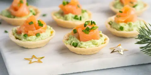 Aperitivos baratos para mucha gente: canapés de salmón y aguacate, decorados con cebollino y estrellas doradas.