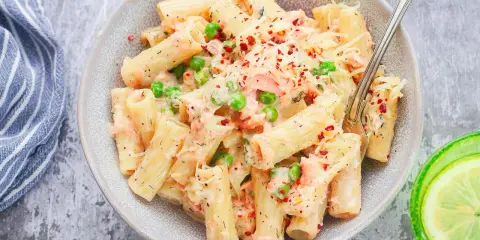 Pyszne danie z makaronem rigatoni, kawałkami łososia, groszkiem i kremowym sosem, posypane serem i płatkami chili. Idealna pasta z łososia na obiad.