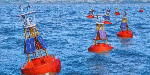 Plusieurs bouées de navigation solaires orange flottent sur une mer bleue agitée. Ces balises bateau guident les navires.