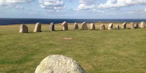 Rząd kamieni Ales Stenar na trawiastym polu, z morzem i chmurami w tle.