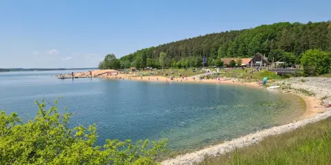 Sonniger Strandtag am Rothsee bei Heideck, Bayern. Menschen entspannen sich am Sandstrand, während Segelboote auf dem Wasser gleiten.