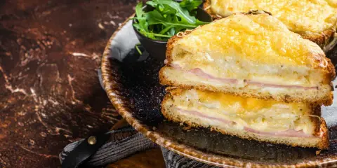 Deux croque monsieur bechamel dorés, garnis de jambon et de fromage fondant, servis avec une salade verte.