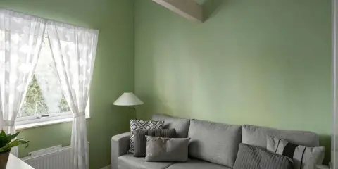 Sofá gris con cojines, lámpara y cortinas blancas junto a pared verde. ¡Excelentes ideas pintar casa con este tono fresco!