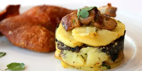 Plat de pommes de terre en millefeuille avec du foie gras et des champignons, accompagné de volaille rôtie.