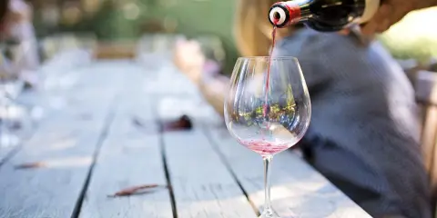 Czerwone wino nalewane z butelki do kieliszka na drewnianym stole.