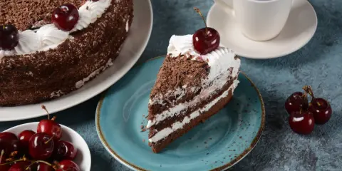 Una porción de tarta Selva Negra, con capas de bizcocho de chocolate, nata y cerezas, decorada con virutas de chocolate y una cereza encima.