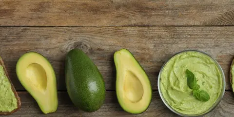 Avocado lagern: Ganze und halbe Avocados, Guacamole in einer Schüssel und Avocado-Toast auf Holzuntergrund.